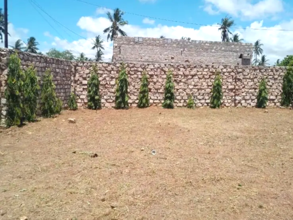 Secure flat plot for sale in Mavueni, Kilifi, featuring a coral stone perimeter wall, heavy gate and convenient access to the Malindi Highway and Kilifi Town.
