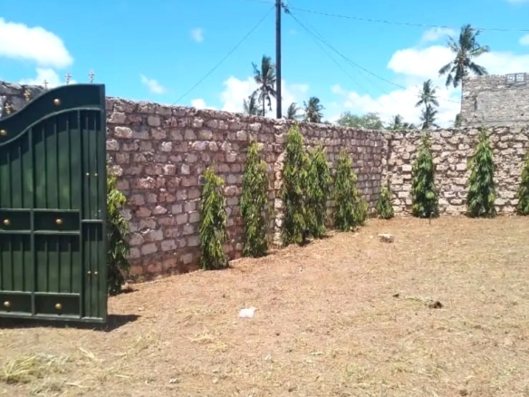 Secure flat plot for sale in Mavueni, Kilifi, featuring a coral stone perimeter wall, heavy gate and convenient access to the Malindi Highway and Kilifi Town.